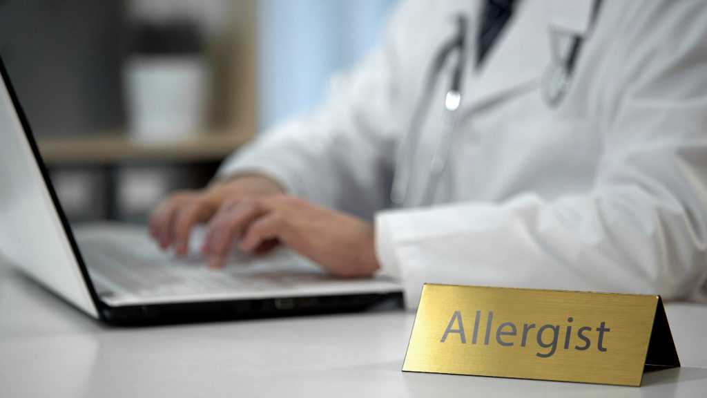 Male allergist prescribing medication in clinic, keeping records, health care