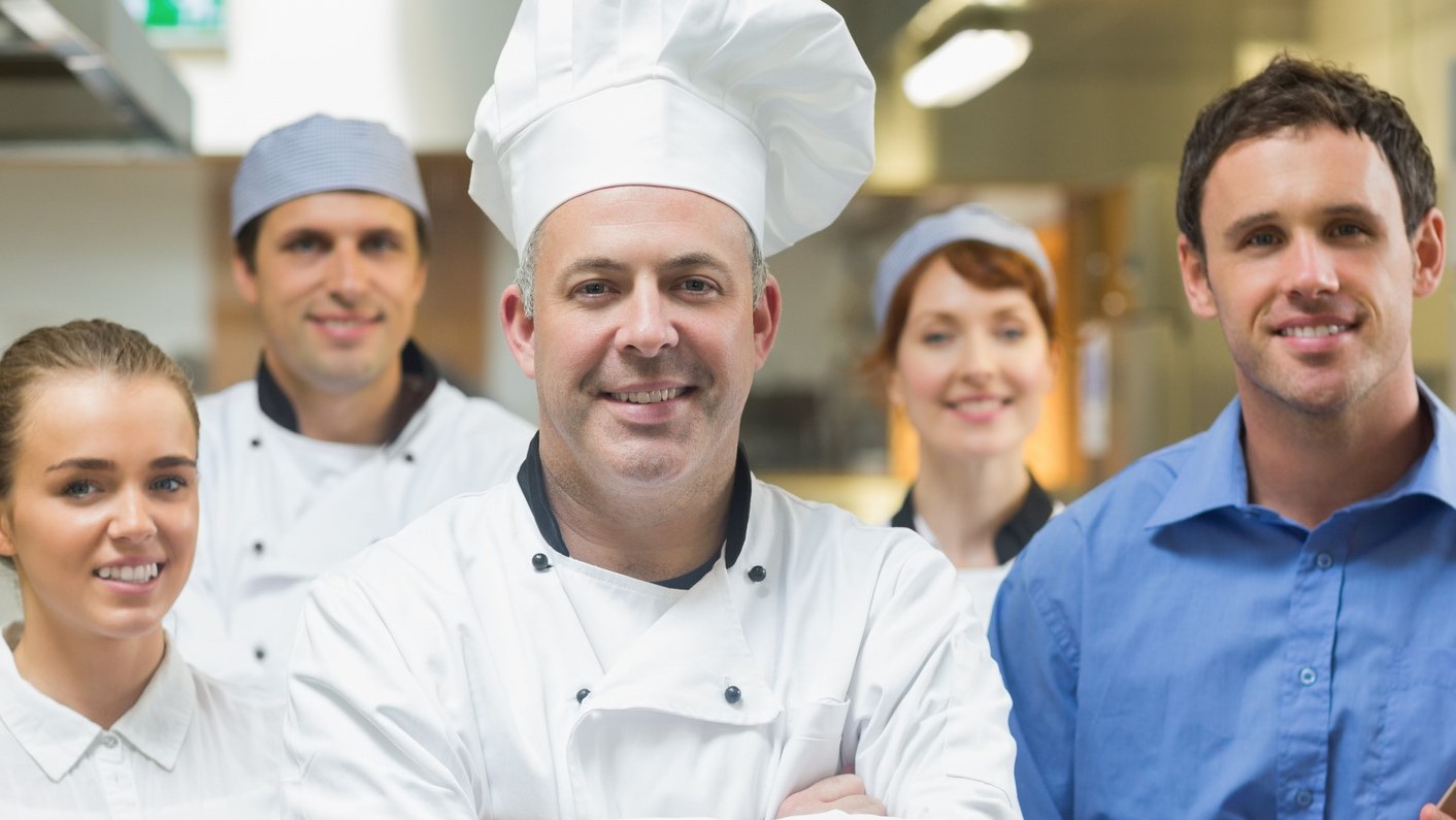 Head chef posing with the team behind him in a profesional kitchen
