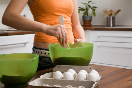 Teen girl mixing baking ingredients in a green bowl, with a carton of eggs on the table.