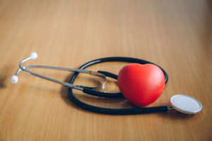 Black stethoscope and heart shaped stress ball on wooden table