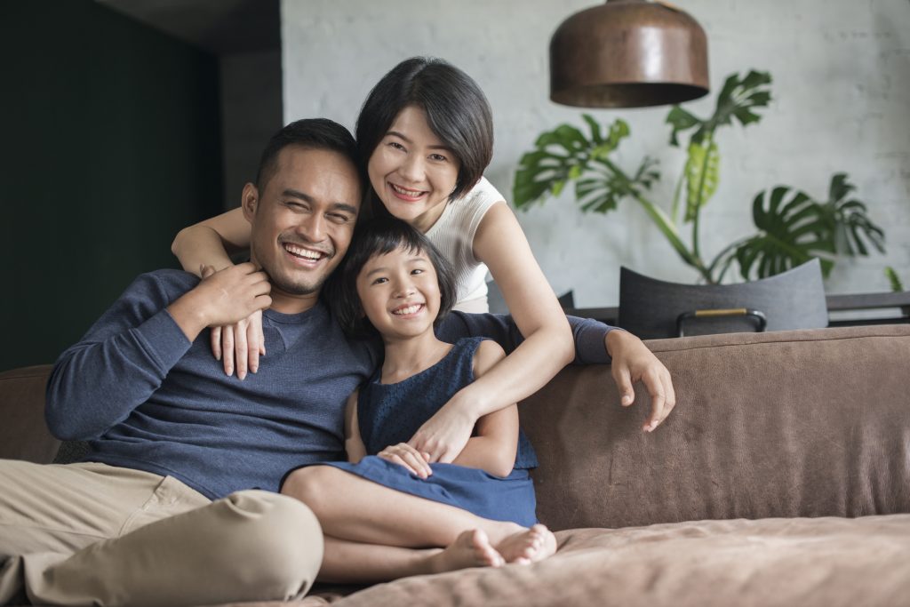 Young Asian parents with only child relaxing on the sofa in the living room.