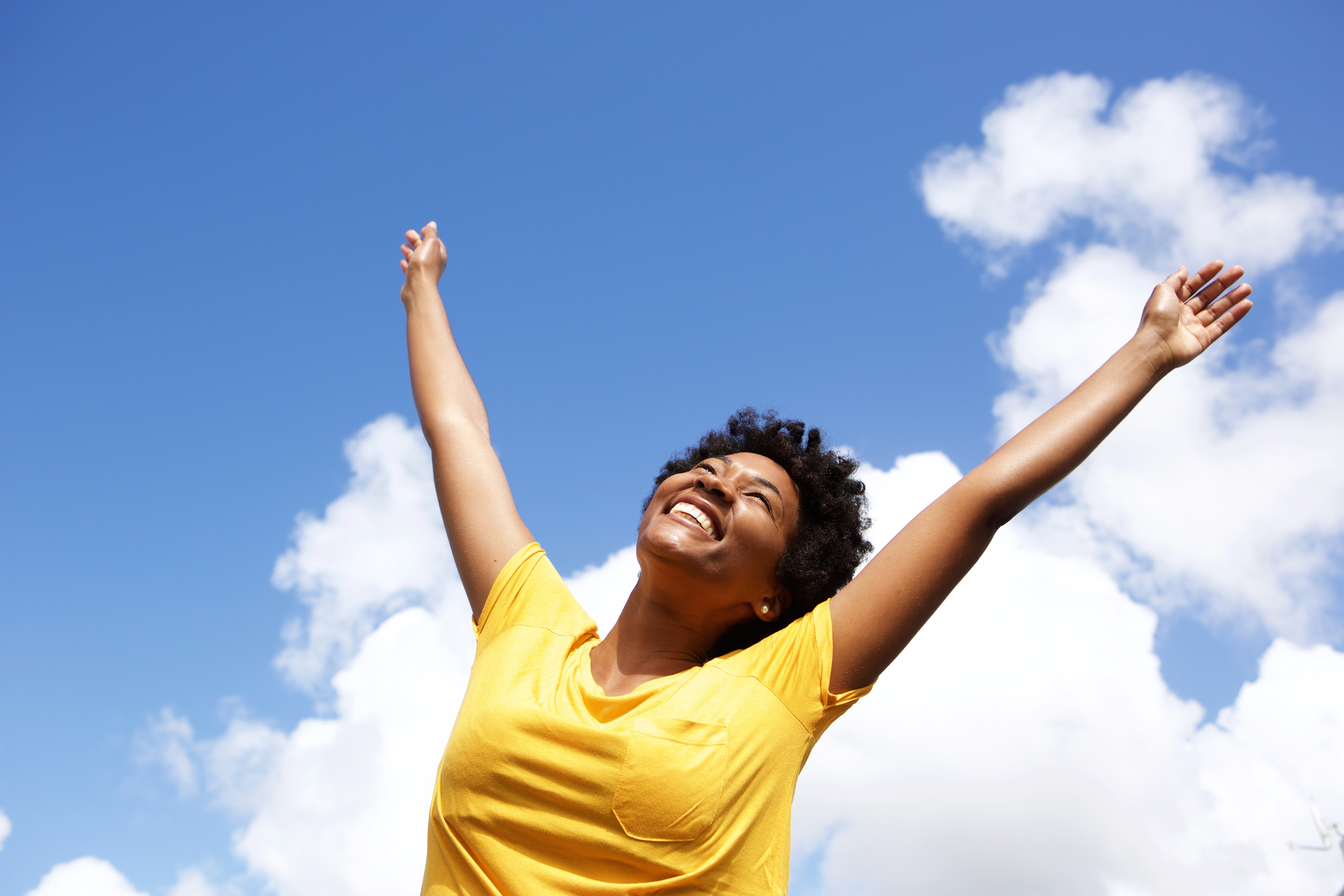 Portrait of cheerful young woman standing outside with her hands raised towards sky