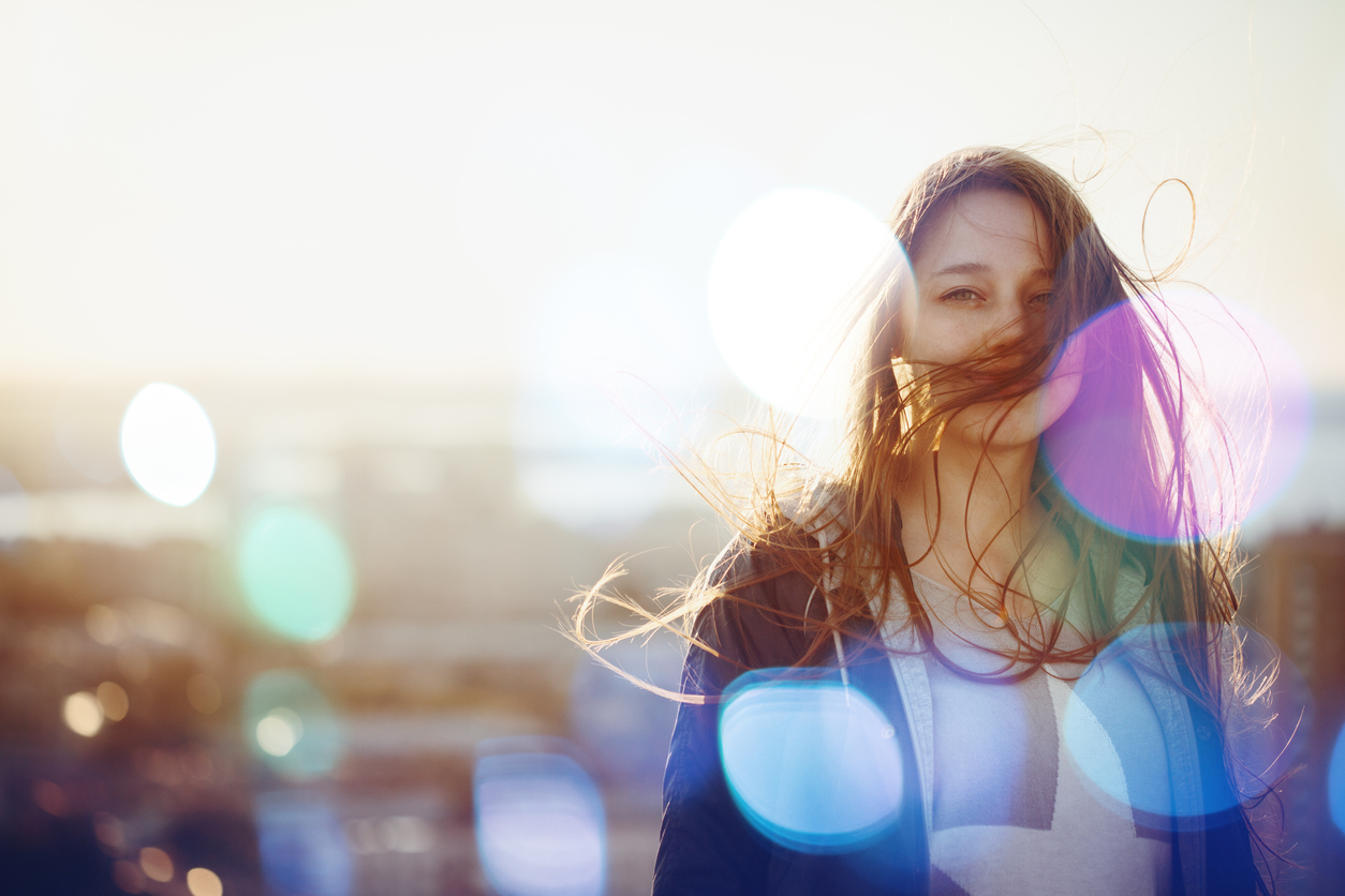Young Woman Standing in Sunset Light, Looking at Camera. Hair Fluttering in the Windi. Selective Focus, Bokeh Lights.
