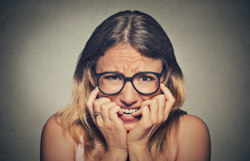 Closeup portrait nervous stressed young woman girl in glasses student biting fingernails looking anxiously craving something isolated on grey wall background. Human emotion face expression feeling