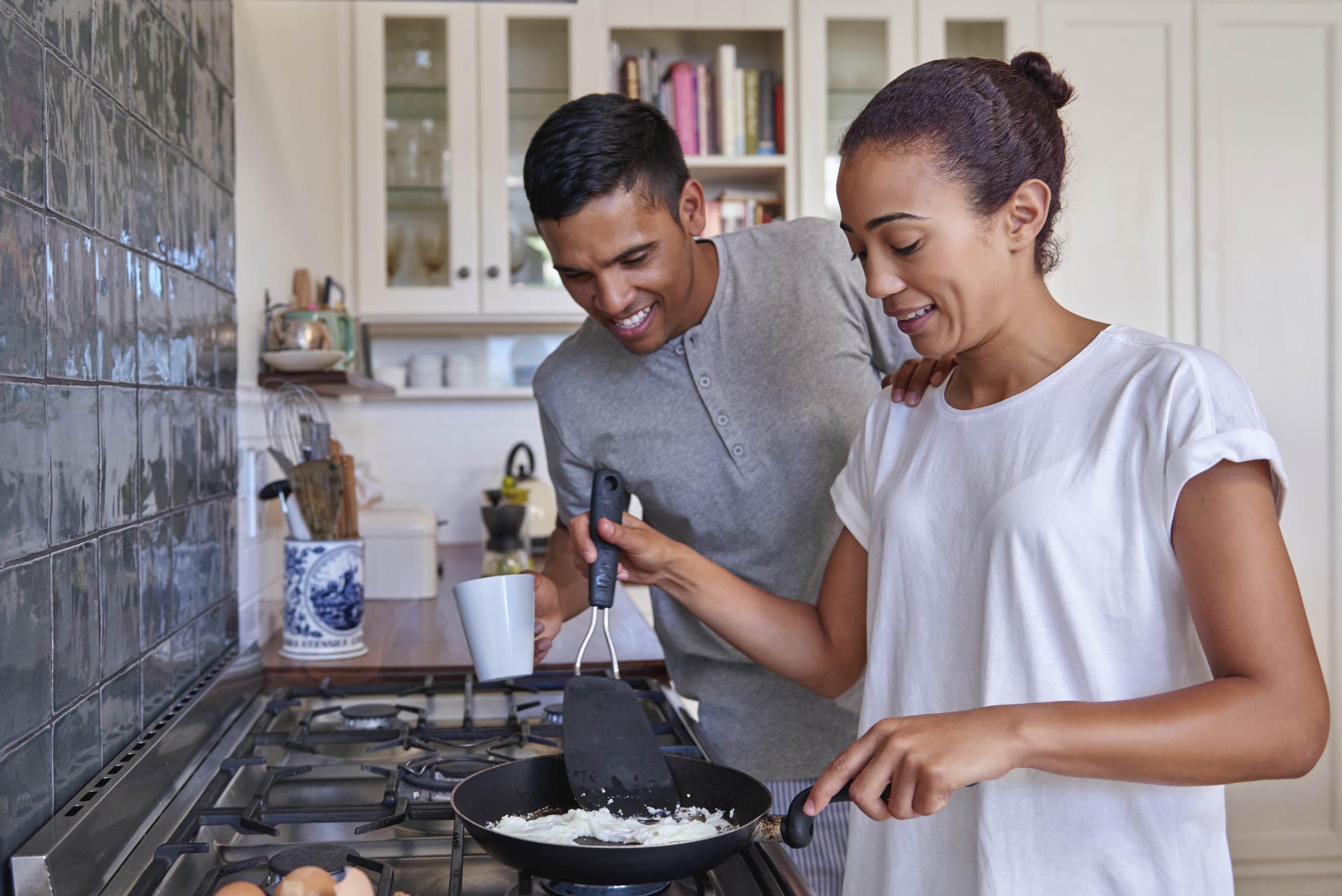 young couple preparing early morning eggs breakfast on stove in home kitchen