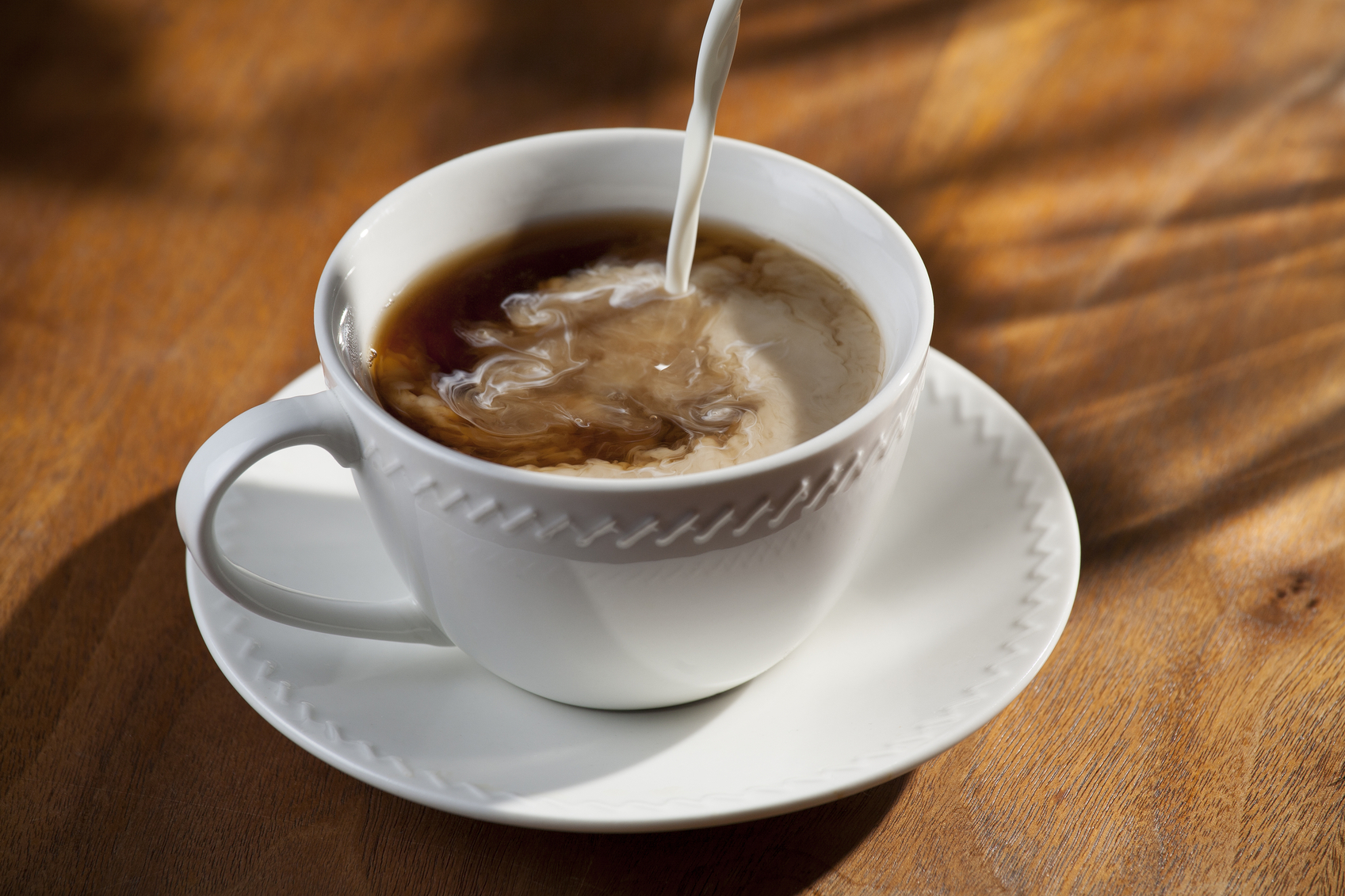 horizontal photograph of a cup of coffee with creamer being poured into it