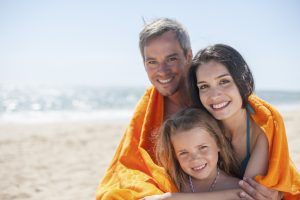 family of three people at the seaside sheltering under a beach towel