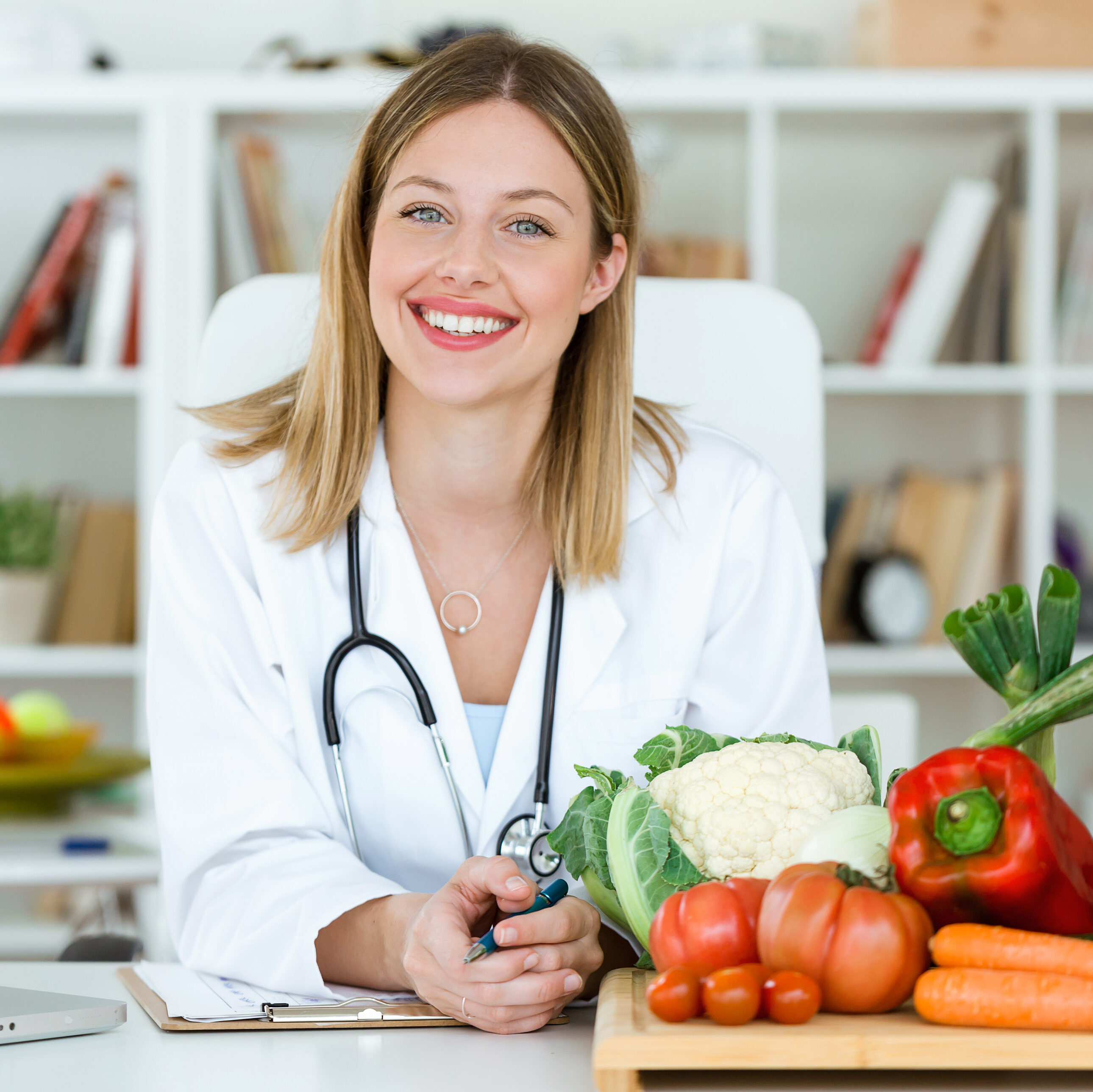 Portrait of smiling nutritionist looking at camera and showing healthy vegetables in the consultation.