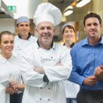 Head chef posing with the team behind him in a profesional kitchen