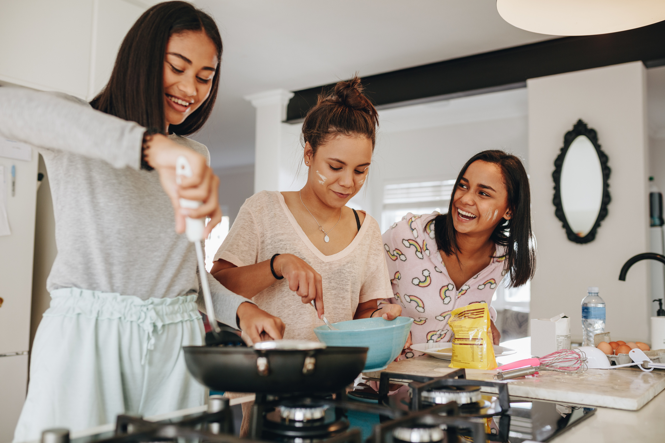 Three girls making food together standing in kitchen