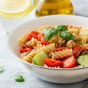 Whole wheat pasta salad with cucumbers, cherry tomatoes, salted salmon and capers on concrete background. Selective focus.