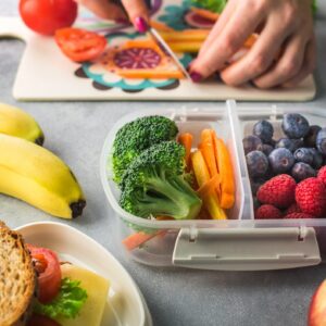 Mother giving healthy lunch for school hands. Fruit and veggies