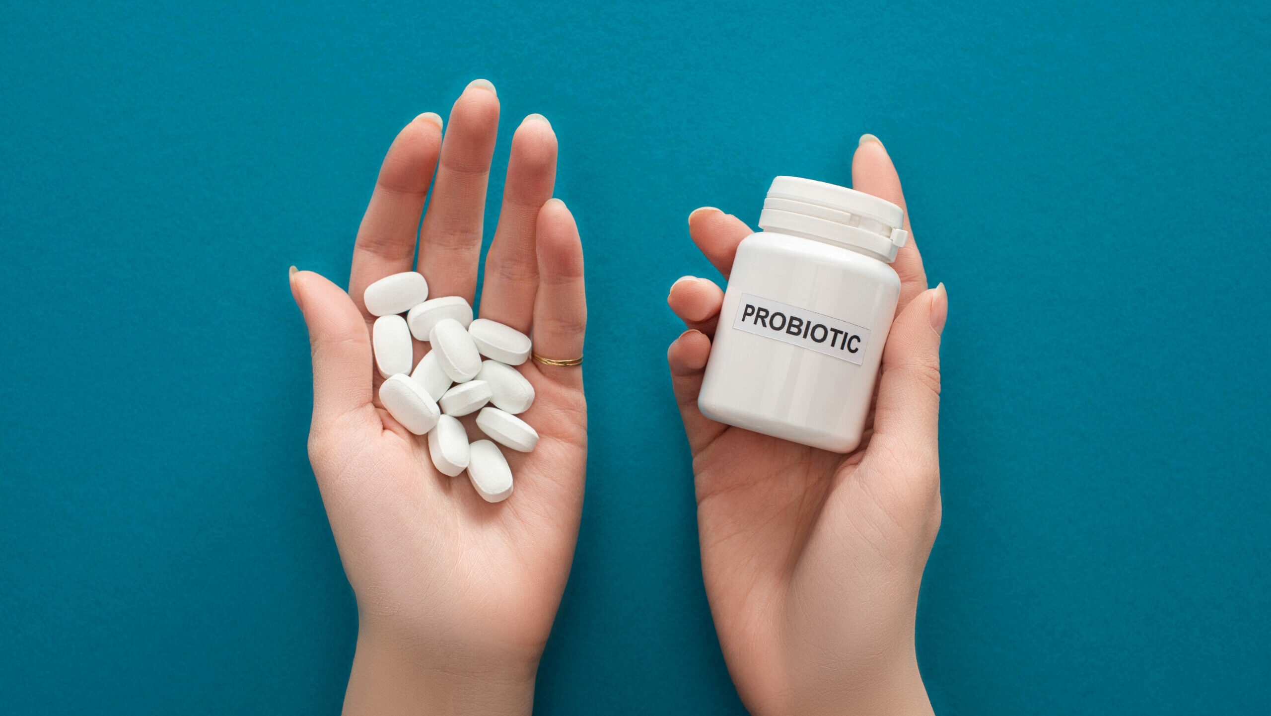 cropped view of woman holding white probiotic container and pills in hands on blue background
