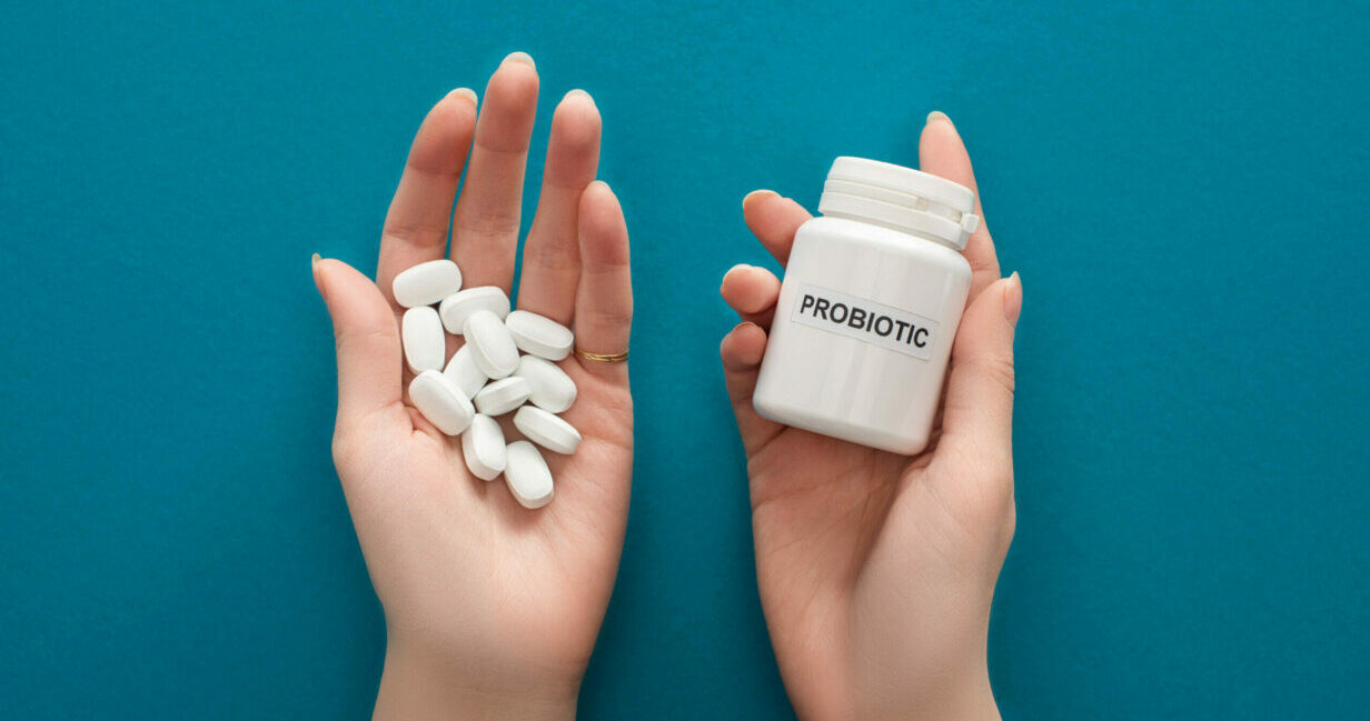 cropped view of woman holding white probiotic container and pills in hands on blue background