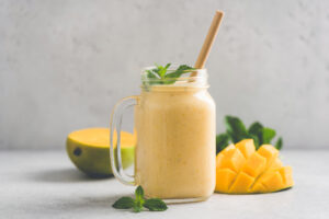 Delicious mango smoothie in glass jar on grey background with copy space. Refreshing summer drink