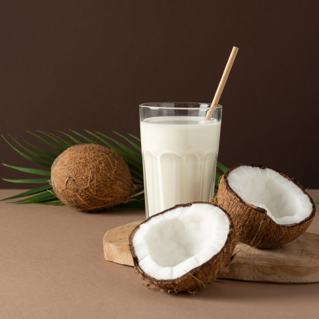 Coconut milk with halves of coconuts over brown background.
