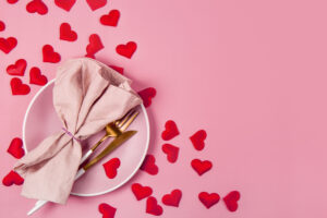 Valentines day table setting on a pink background top view, photo with copyspace. A pink plate, golden cutlery and red hearts top view, romantic dinner concept. High quality photo