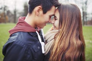 A male teen and a female teen in a close embrace with foreheads touching