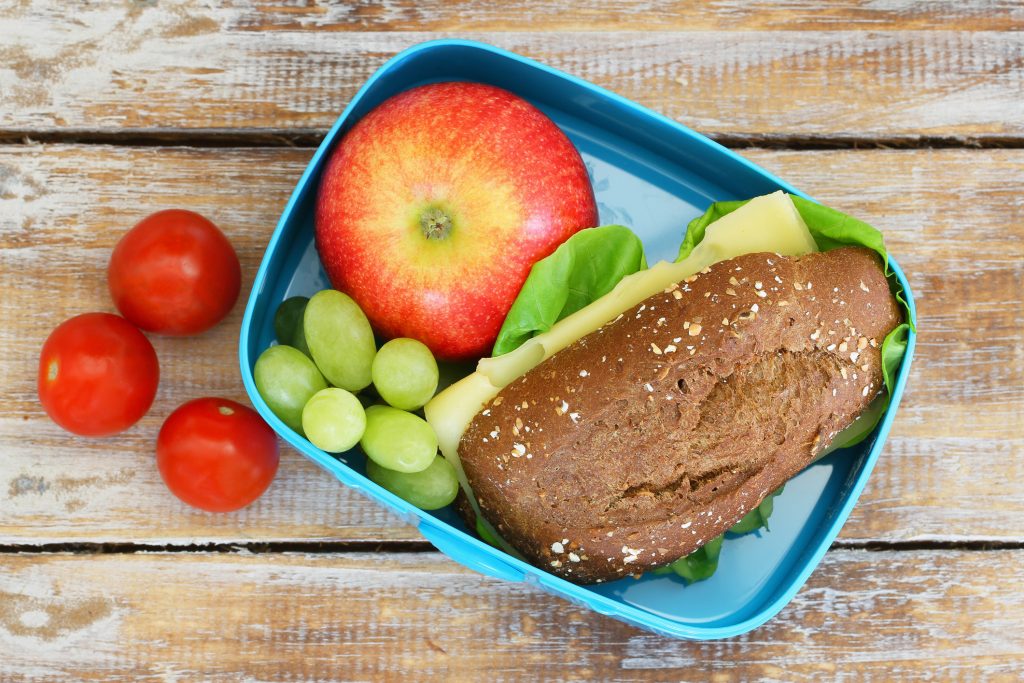 Lunch box consisting of wholegrain cheese sandwich, apple, grapes and cherry tomatoes