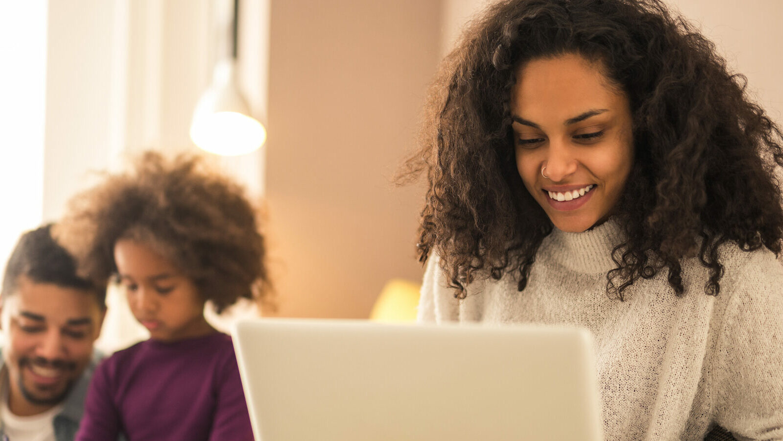 Mother on laptop while dad and daughter having fun.