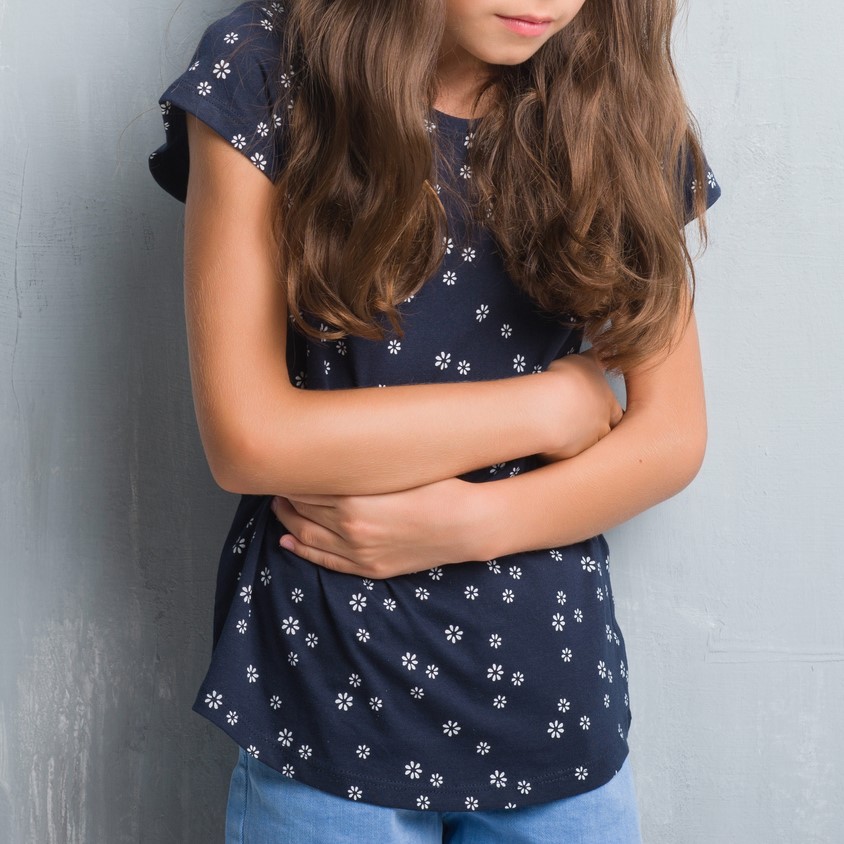 Young girl over grunge grey wall with hand on stomach because indigestion, painful illness feeling unwell. Ache concept.